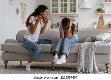Angry mad mother trying to discipline child, expressing frustration shouting at teenage daughter sitting on sofa covering ears with hands. Psychological effects of yelling at kids, verbal abuse - Shutterstock ID 2223557457