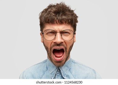 Wütende männliche Schreie wütend, hält den Mund weit geöffnet, fühlt schreckliche Schmerzen, gekleidet in einem Jean-Shirt. Indigene Europäer schreien aggressiv, in Panik, einzeln auf weißem Hintergrund.