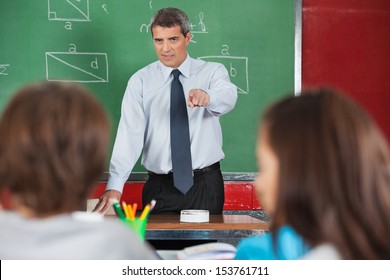 Angry Male Teacher Pointing At Students In Classroom