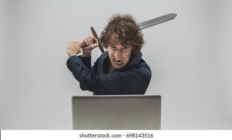 Angry Man About To Destroy His Laptop Computer By Hitting It With A Medieval Sword With An Intense Expression Of Rage - Concept Of Computer Hassles And Worries