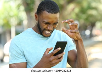 Angry man with black skin checking smart phone content in a park