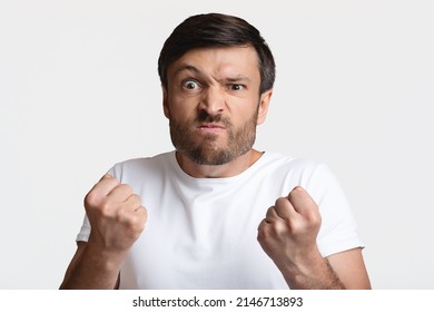 Angry Man Clenching Fists Ready To Fight Looking At Camera Standing Over White Background In Studio. Male Aggression, Anger And Rage, Negative Emotions Concept