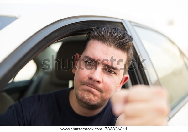 Angry man driver pissed off by drivers in front of\
him and gesturing with hands. Angry young man driving a vehicle is\
expressing his road rage.