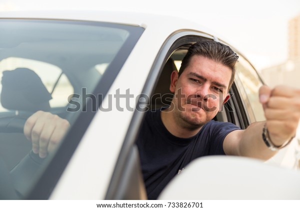 Angry man driver pissed off by drivers in front of\
him and gesturing with hands. Angry young man driving a vehicle is\
expressing his road rage.