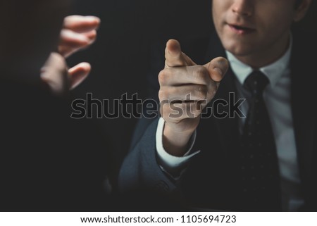 Angry man in formal business suit pointing hand to somesone he talking to in dark interrogation room