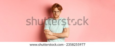 Angry man in glasses with red hair frowning, cross arms on chest in defensive pose, sulking at you, standing over pink background.