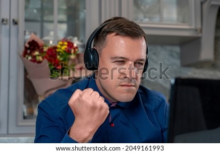 Angry man with headphones clenched his fist, looking at laptop screen, writes offensive comments to haters, spreads fake rumors, feeds trolls online. Concept hate, trolling, anger on Internet forum