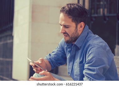 Angry Man Looking At His Mobile Phone Sitting On Steps Outside Apartment Complex 