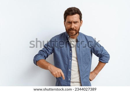 Angry man points finger down and say to you come here right now while standing on white background