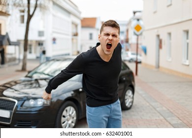 Angry Man Screams Near A Car In The City. The Concept Of Anger