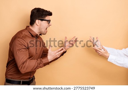 Angry man shouting and gesturing toward another person off-frame, showing frustration, confrontation and emotional tension during a heated disagreement in a neutral studio setting.