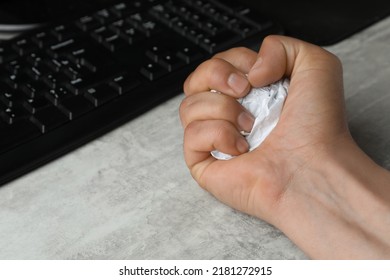 Angry Man Squeezing Paper Near Computer Keyboard At Table, Closeup