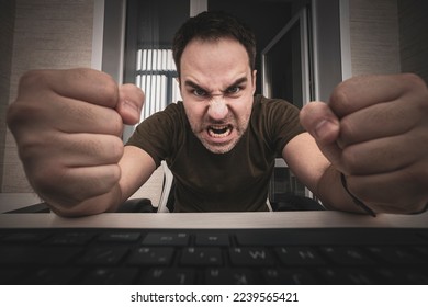 angry man swearing and cursing against information technology and his compuiter worries and hassles - concept of hating computers. freelancer punches the keyboard. - Shutterstock ID 2239565421