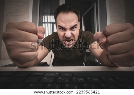 angry man swearing and cursing against information technology and his compuiter worries and hassles - concept of hating computers. freelancer punches the keyboard.