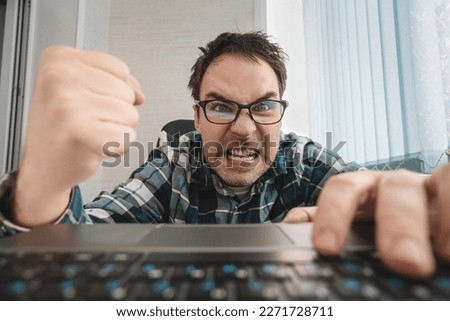 angry man swearing and cursing against information technology and his compuiter worries and hassles - concept of hating computers. businessman in a shirt in the office punches the keyboard.