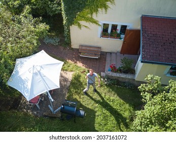 Angry man upset by flying drone over his garden. The concept of spying on neighbors and their privacy. Man trying to knock down  drone from sky over his own garden with broom. Breaking rules flying 