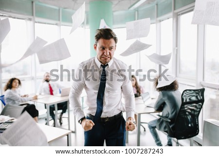 Angry manager in white shirt standing angrily at his desk. Throwing papers.