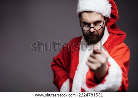 Angry mature Santa Claus in traditional red costume showing fig over dark studio background. Spoiled christmas and no presents.