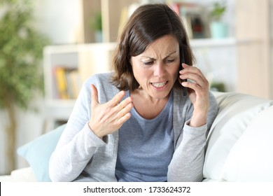 Angry middle age woman arguing calling on smart phone sitting on a couch at home - Powered by Shutterstock