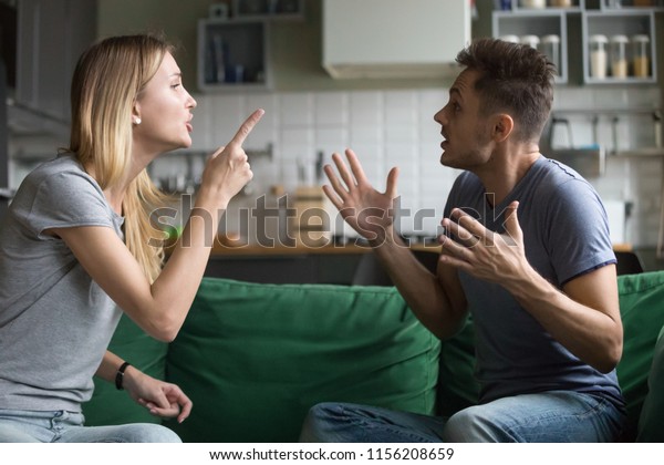 Angry millennial couple arguing shouting blaming\
each other of problem, frustrated husband and annoyed wife\
quarreling about bad marriage relationships, unhappy young family\
fighting at home concept