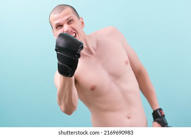 An angry MMA fighter in black gloves hitting an uppercut on a blue background. Ready to make a punch. Hand. Aggression. Athlete. Fist. Force. Martial. Muscle. Workout. Aggressive. Man. Young
