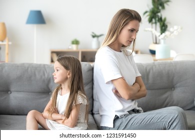 Angry mother and little child girl sitting back to back on sofa not talking after fight, stubborn kid preschool daughter and annoyed mom ignoring each other upset by argument, family conflict concept