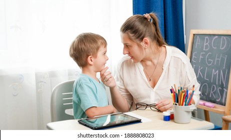 Angry Mother Looking And Talking To Her Silly Little Son Doing Homework At Home. Conflict Between Parent And Child