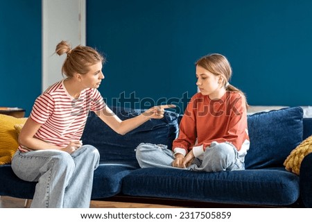 Angry mother pointing upset child sitting on sofa in living room. Conflict children and parents.Toxic mom humiliates young girl for bad behavior. Difficulties in raising teenage daughter