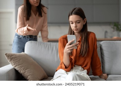 Angry mother shouting and arguing with teenage daughter over use of mobile phone, girl sitting on sofa at home, ignoring mom - Powered by Shutterstock