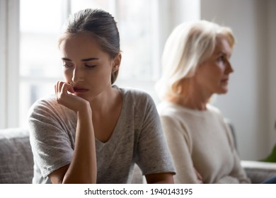 Angry offended senior Caucasian mother and adult grownup daughter sit separate at home ignore talking after family fight. Unhappy mature mom and child avoid speaking. Generation gap concept.
