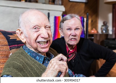 Angry Old Couple Sitting Indoors With Scowling Expression
