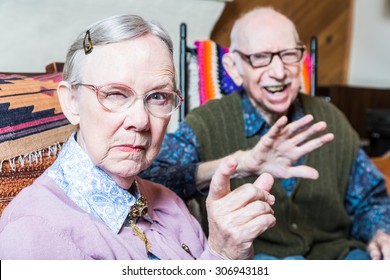 Angry old couple sitting in living room woman pointing