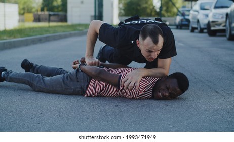 Angry police officer interrogating African American guy on ground