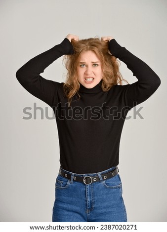 Angry pretty Caucasian blonde woman holding her tousled hair with her hands. Studio shot.