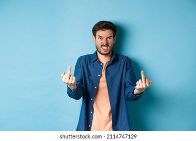 Angry Rude Guy Showing Middle Finger And Saying Fuck You, Swearing And Staring Furious At Camera, Standing On Blue Background