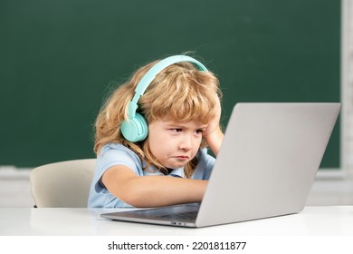 Angry Sad Child Boy In Headphones Using A Laptop And Study Online With Video Call Teacher At School. Little Funny System Administrator Or Programmer.