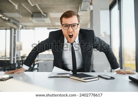 Angry senior businessman sitting at his desk and screaming.