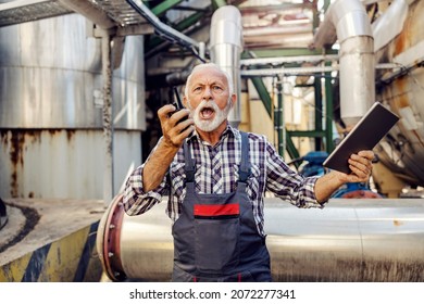 An angry senior supervisor stands in the factory with a tablet in his hands and yelling over the walkie-talkie. There is no place or time for mistakes. An angry supervisor yelling at his employees.