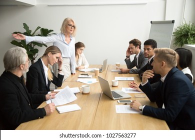 Angry senior woman boss firing unprofessional employee with hand gesture at diverse team meeting, dissatisfied aged female executive dismissing incompetent manager for bad work result in boardroom - Powered by Shutterstock