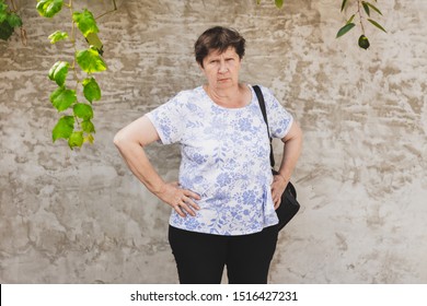 Angry Senior Woman With Grumpy Face Standing With Hand On Her Hips Outdoors - Cute And Funny Old Lady With Moody Temper On The Street