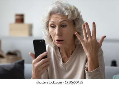 Angry shocked mature phone user staring at screen in surprise. Elderly lady worried about app error, data stealing, scam, bad news, problems with smartphone. Annoyed woman using cell for video call