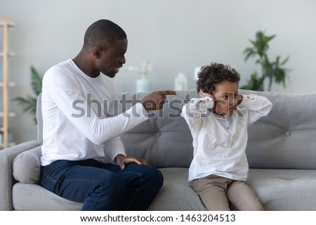 Angry single black father scolding stubborn fussy little african son closing ears not listening ignoring dad punish small mixed race kid boy for bad behavior, parent and child family conflict concept