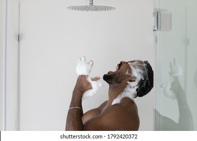 Angry soapy African American young man with white shampoo foam on hair dissatisfied by broken shower, screaming, standing in bathroom, problem with suddenly turned off hot or cold water