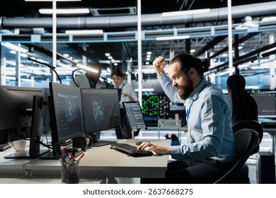 Angry software developer in data center clenching fists while looking at AI visualization interface on monitor. Frustrated technician reacting to artificial intelligence software glitches