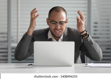 Angry stressed african business man using laptop mad about broken computer online problem annoyed with slow stuck laptop error, crazy about system virus or data loss, outraged with website mistake