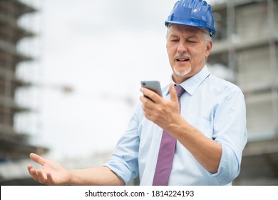 Angry and stressed architect looking at his mobile phone in front of a construction site