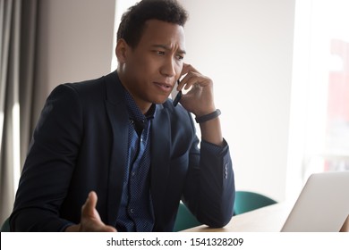 Angry stressed black male businessman disputing on phone with partner. Outraged african american manager, lawyer, banker, consultant or real estate agent listening bad news from client at office.