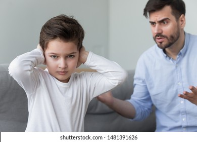 Angry strict father shouting screaming at little son annoyed dad lecturing scolding for discipline rebellious naughty child, focus on boy cover ears with hands not to listen, family conflicts concept