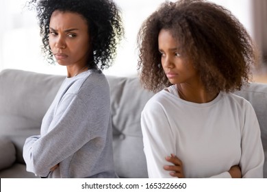 Angry Stubborn African Mother Sister And Teen Child Girl Sitting Back Turned Away On Sofa Not Talking After Quarrel Fight, Upset Teenage Daughter Ignore Annoyed Mom, Family Conflict Puberty Concept