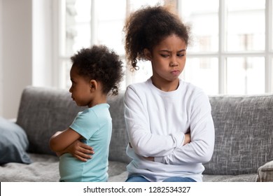 Angry stubborn african preschool girl sister and offended little boy brother ignoring each other sitting on couch feel jealous avoiding talk, 2 children conflict, siblings rivalry bad relationship